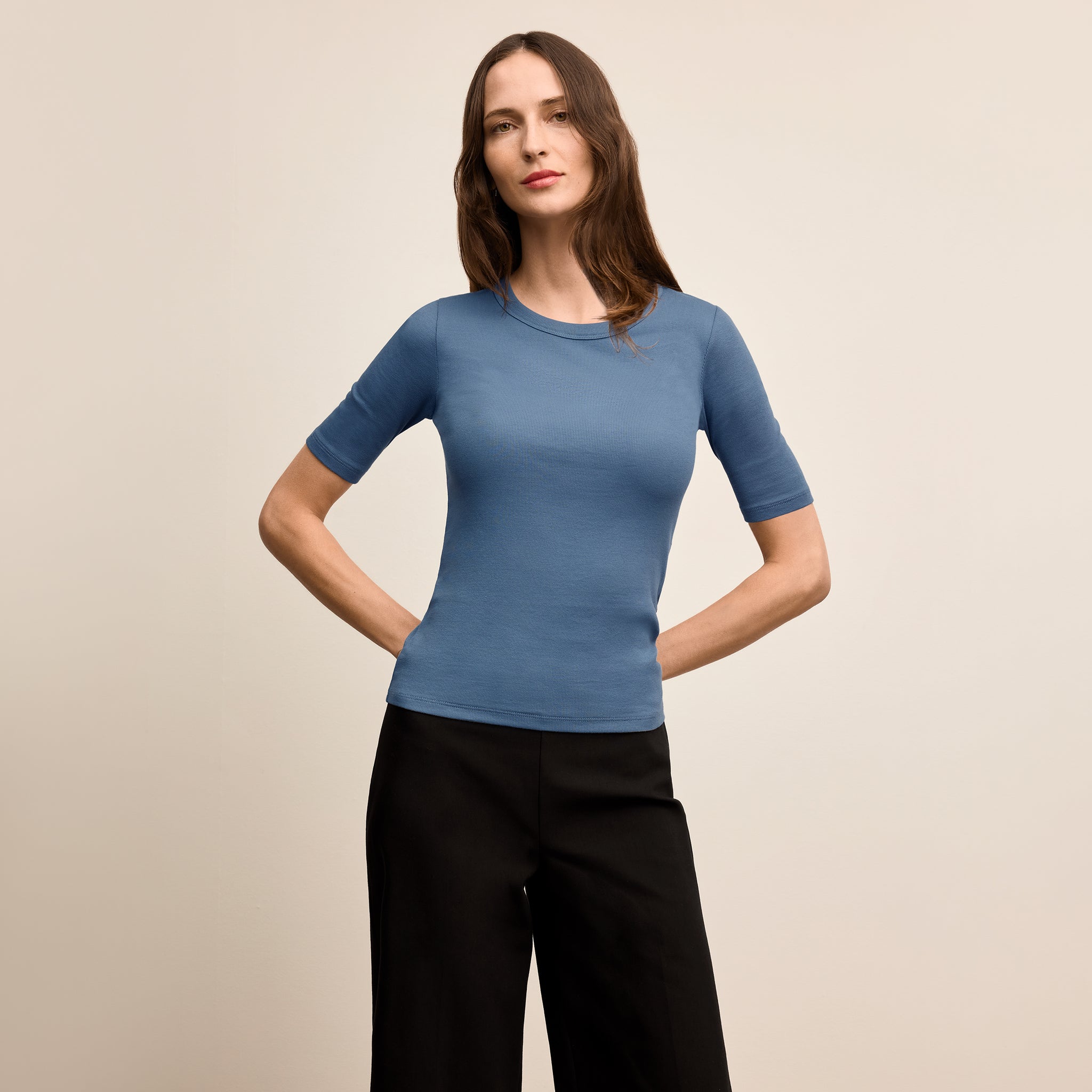 Woman wearing a blue short-sleeve top and black pants on a beige background 
