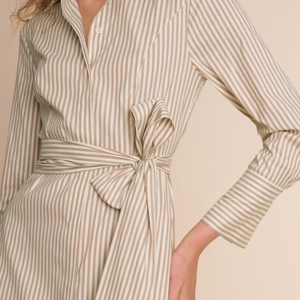 Woman wearing a beige and white striped dress with a tie waist on a beige background