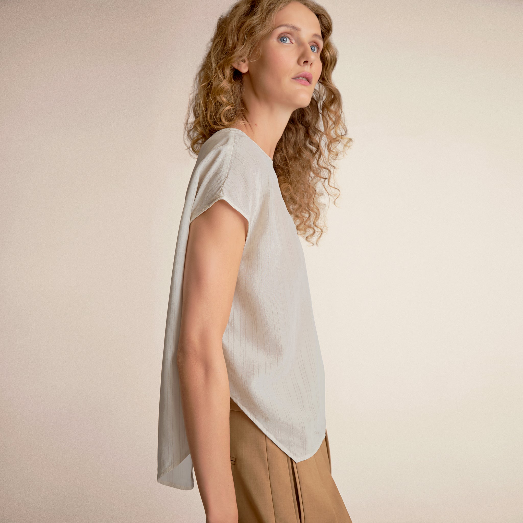 Woman wearing a light-colored blouse and beige pants against a plain background