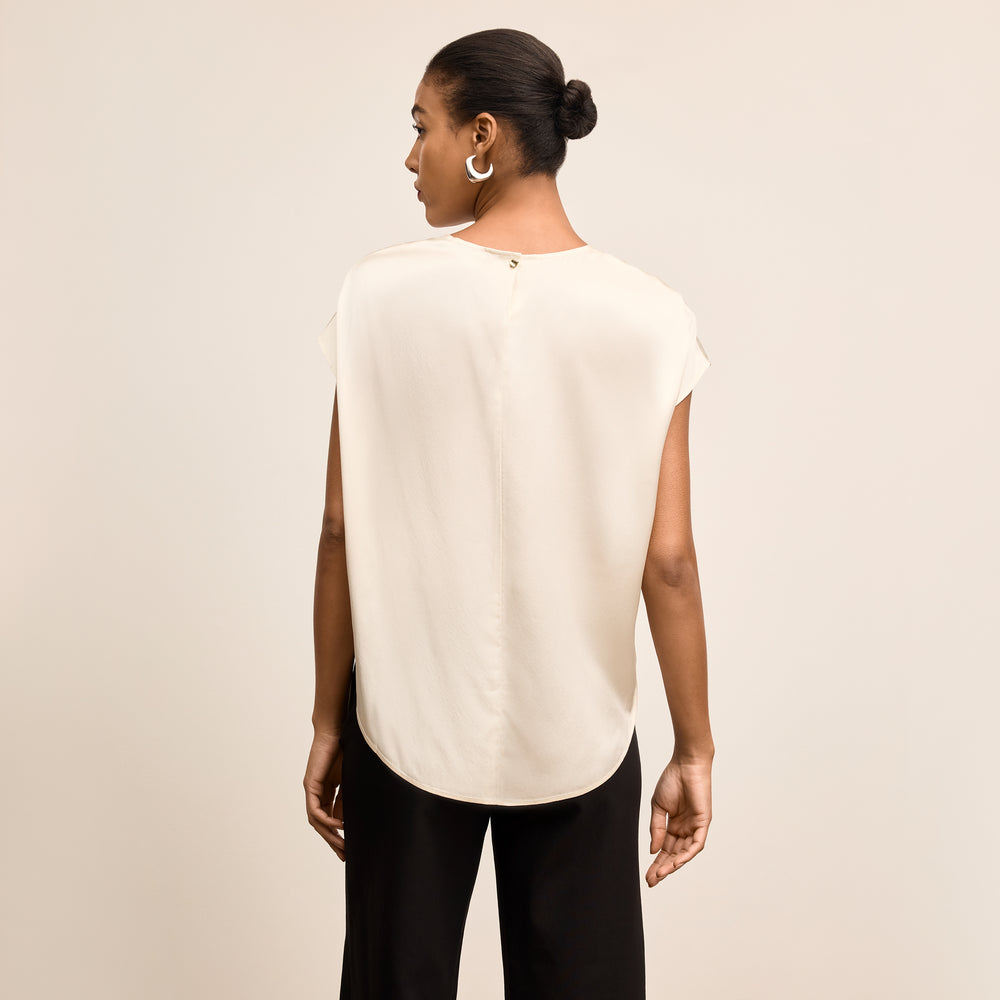 Woman wearing a white sleeveless top and black pants on a beige background