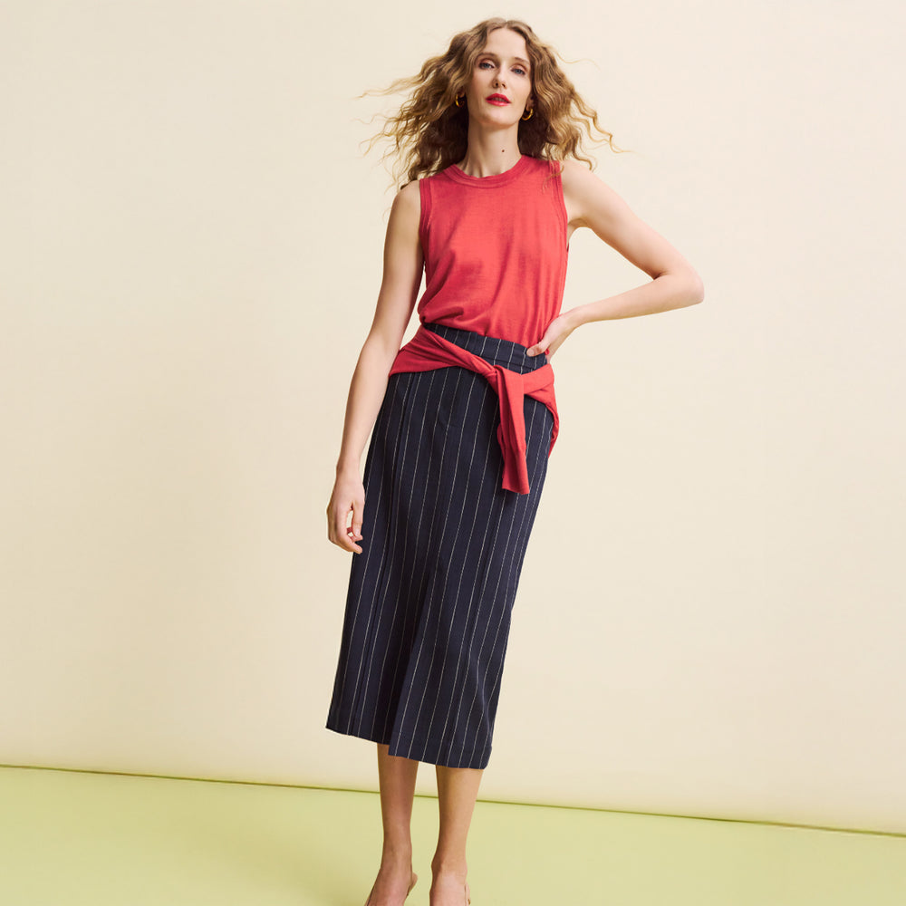 Woman wearing a red sleeveless top and navy pinstripe skirt on a yellow background