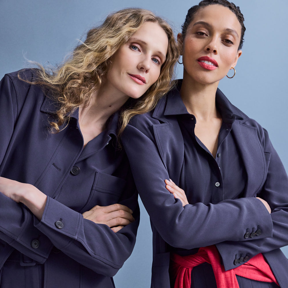 Two women wearing navy blue outfits with a red scarf against a gray background