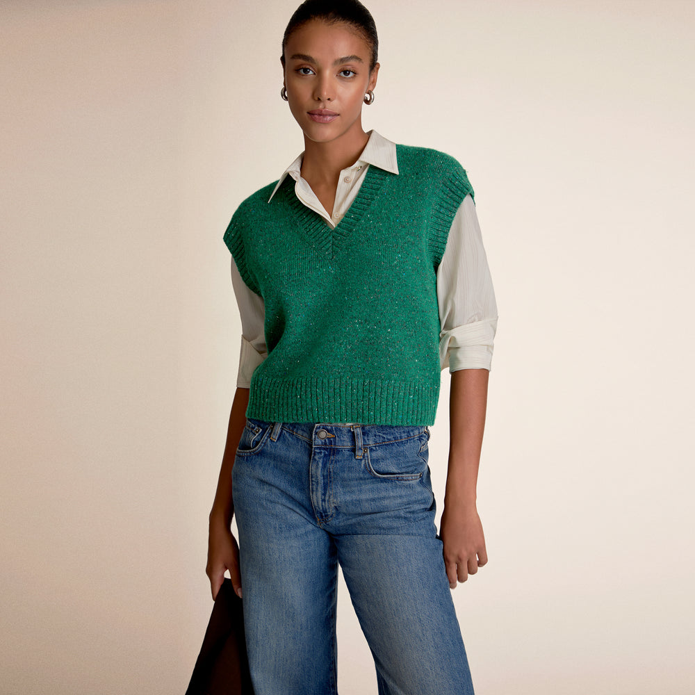 Woman wearing green sweater vest and blue jeans