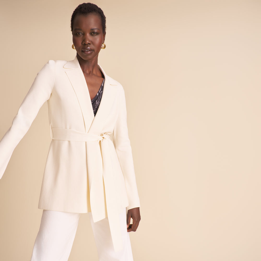 Woman wearing a white blazer with a belt on a beige background