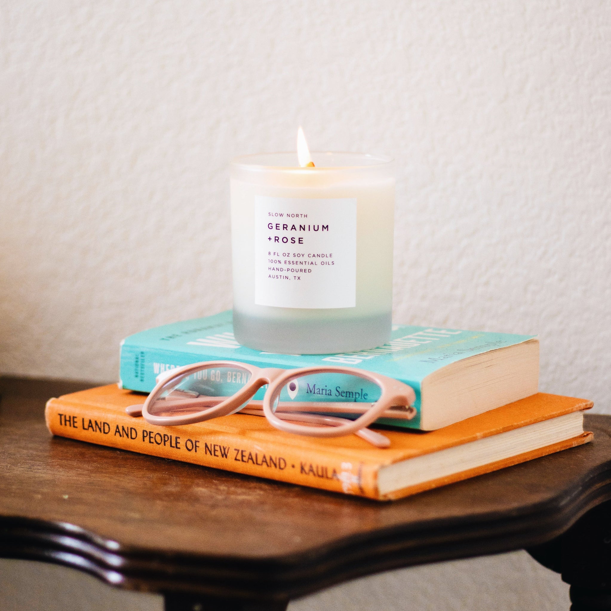 Candle on a stack of books with glasses on top, against a neutral background