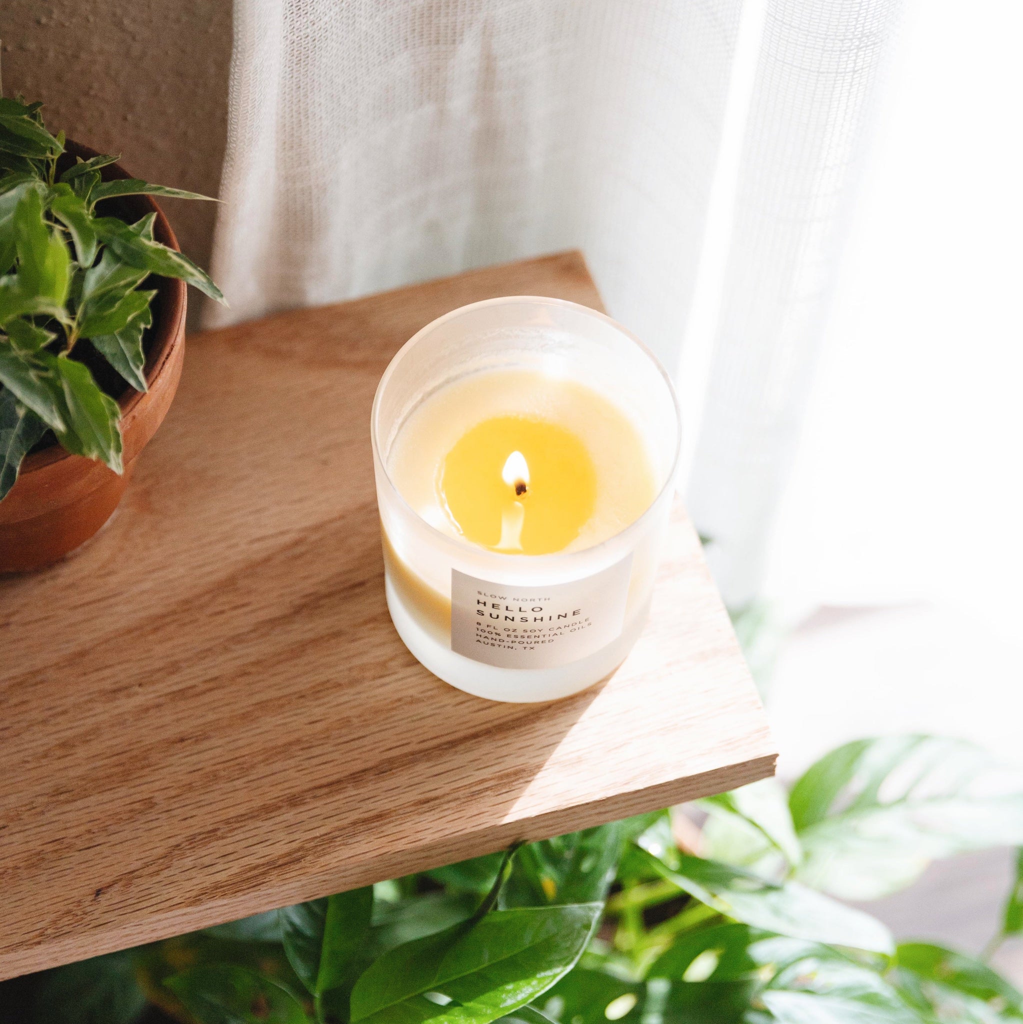 Candle in a glass jar on a wooden surface with plants in the background
