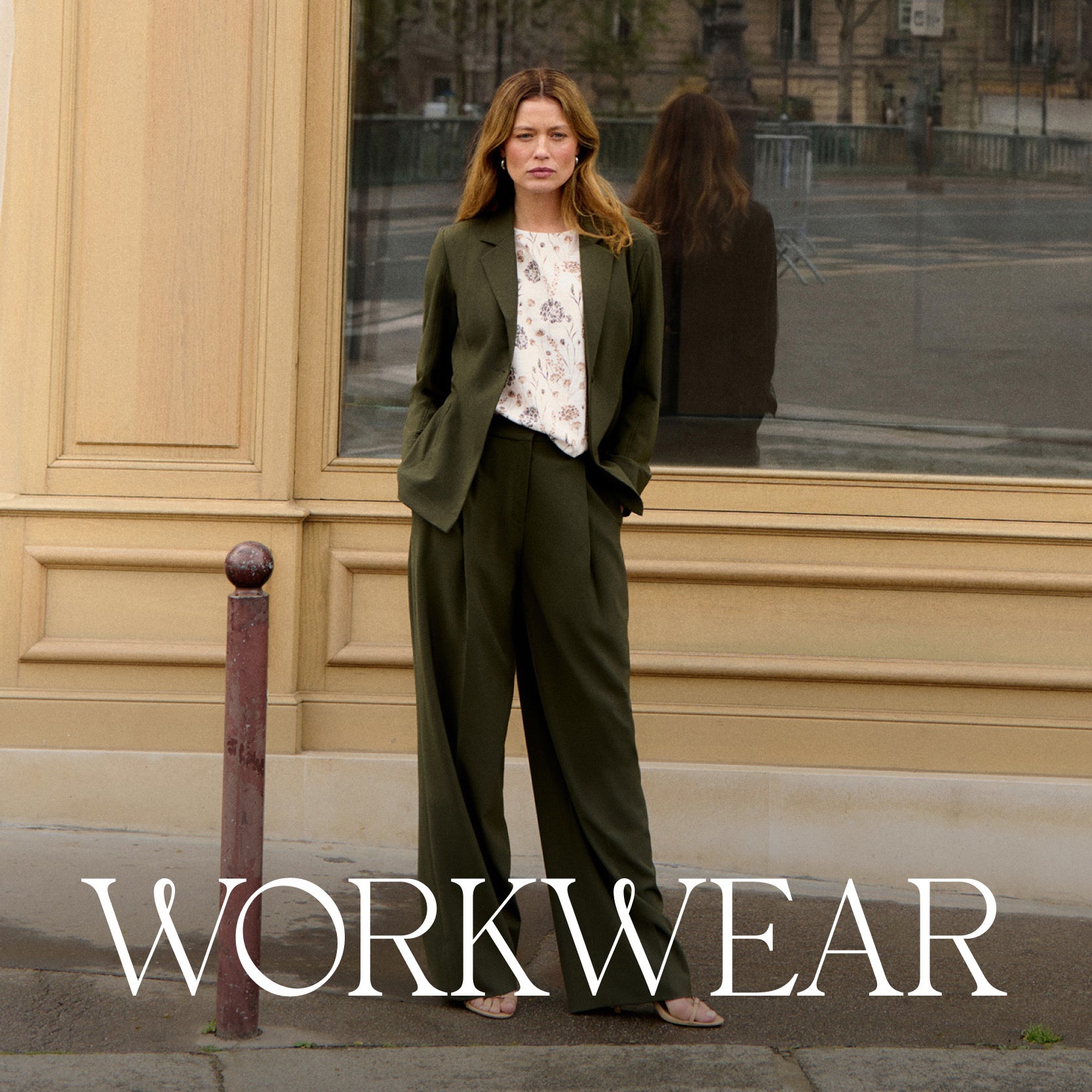 Woman in a green suit standing in front of a reflective building facade with 'WORKWEAR' text overlay.