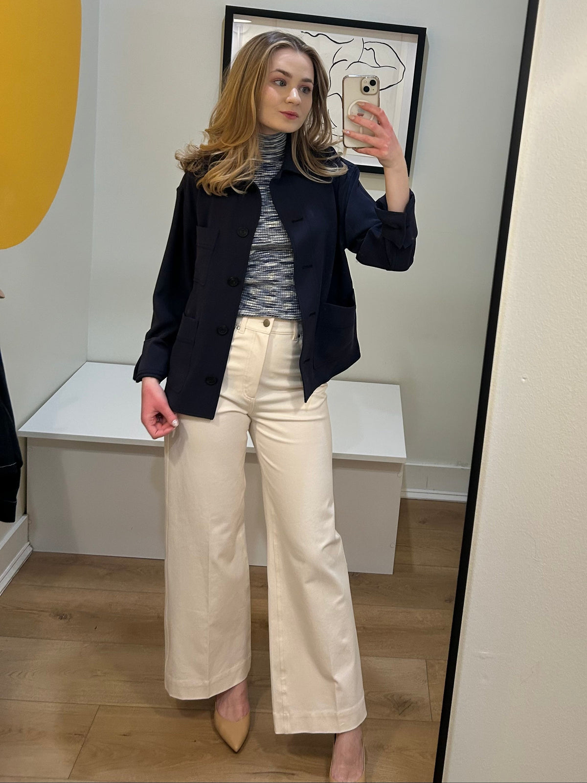 Woman taking a mirror selfie wearing a navy blazer, gray turtleneck, and beige pants.
