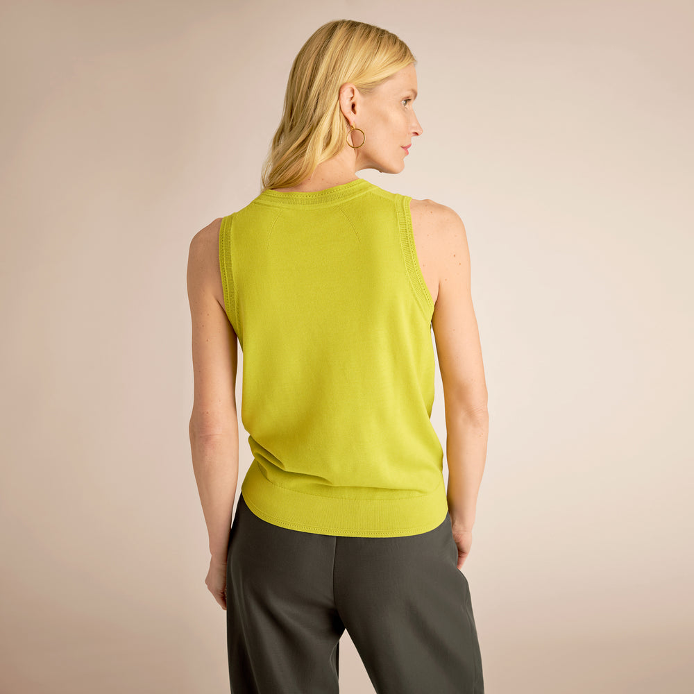 Woman wearing a green sleeveless top and gray pants against a beige background