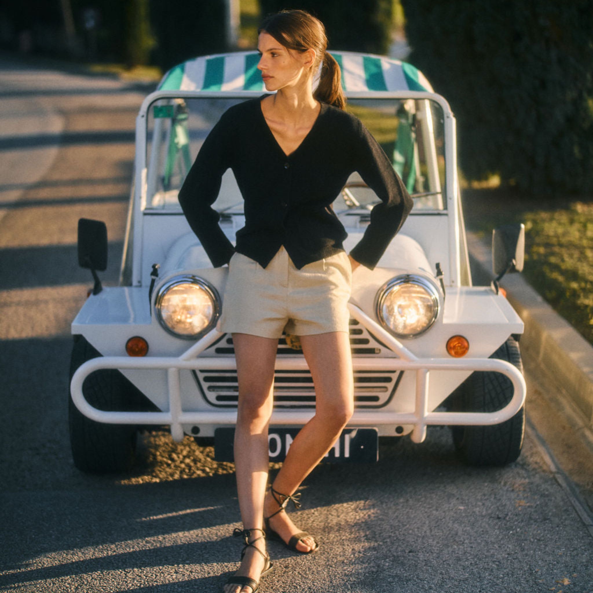 Woman standing in front of a small white vehicle with a green and white striped roof on a road.
