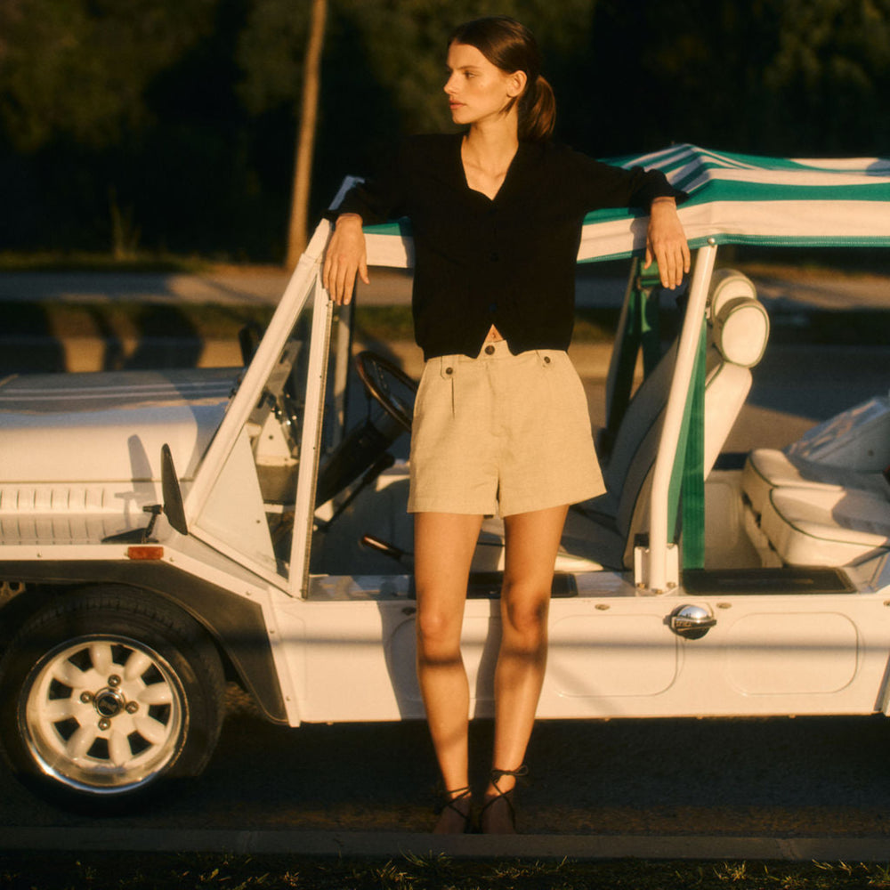 Woman standing next to a vintage car with a striped cover in a natural setting