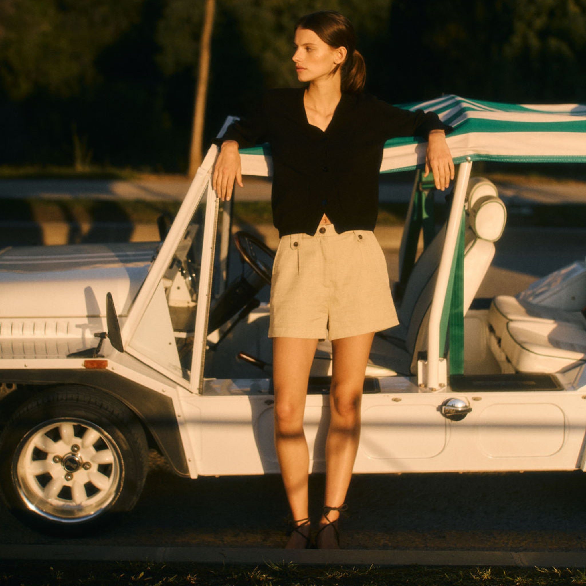 Woman standing next to a vintage car with a striped cover in a natural setting