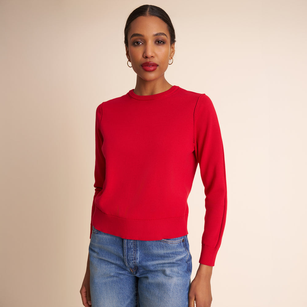 Woman wearing a red sweater and blue jeans against a beige background