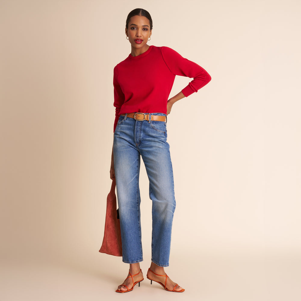 Woman wearing a red sweater and blue jeans on a beige background.