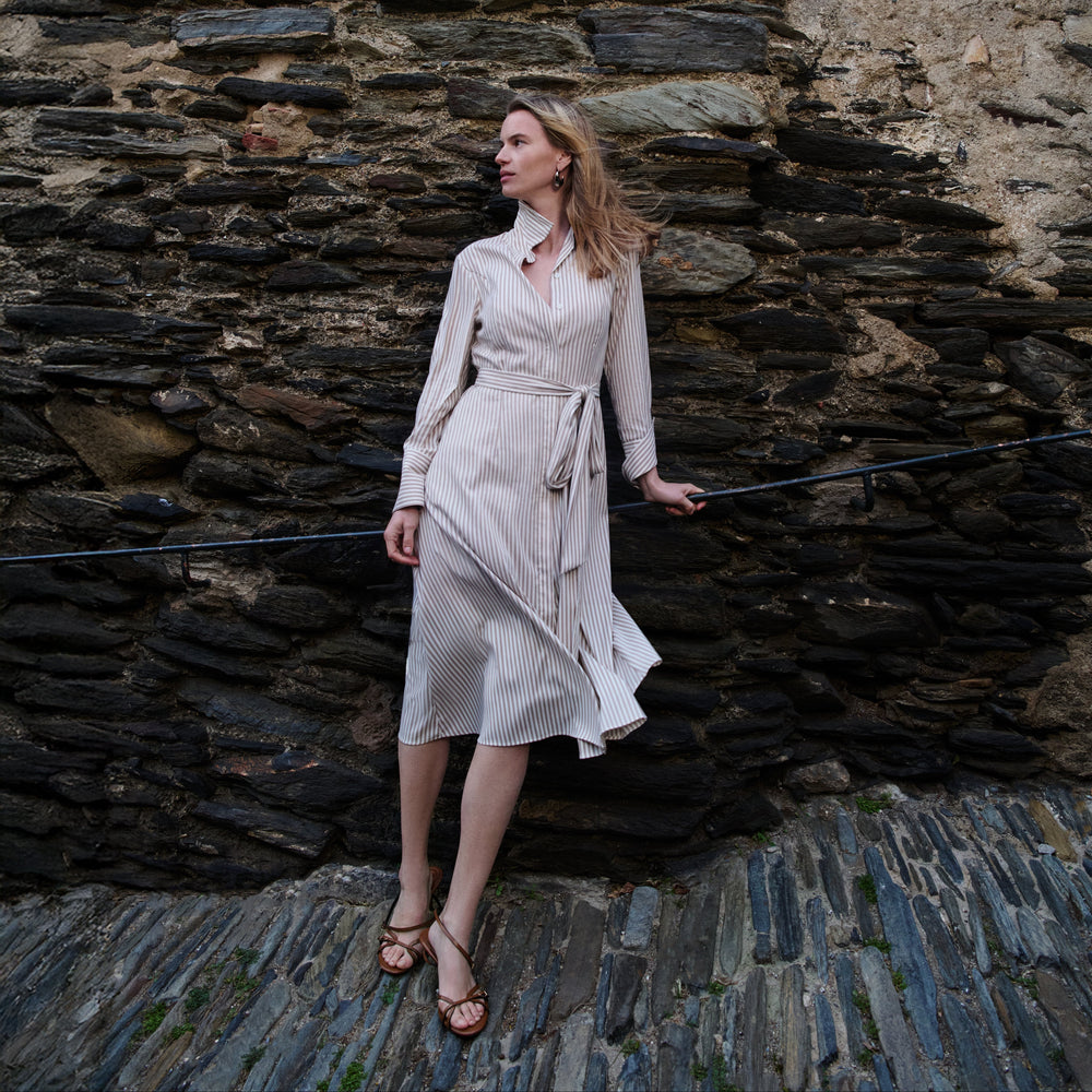 Woman in a white dress standing against a stone wall.