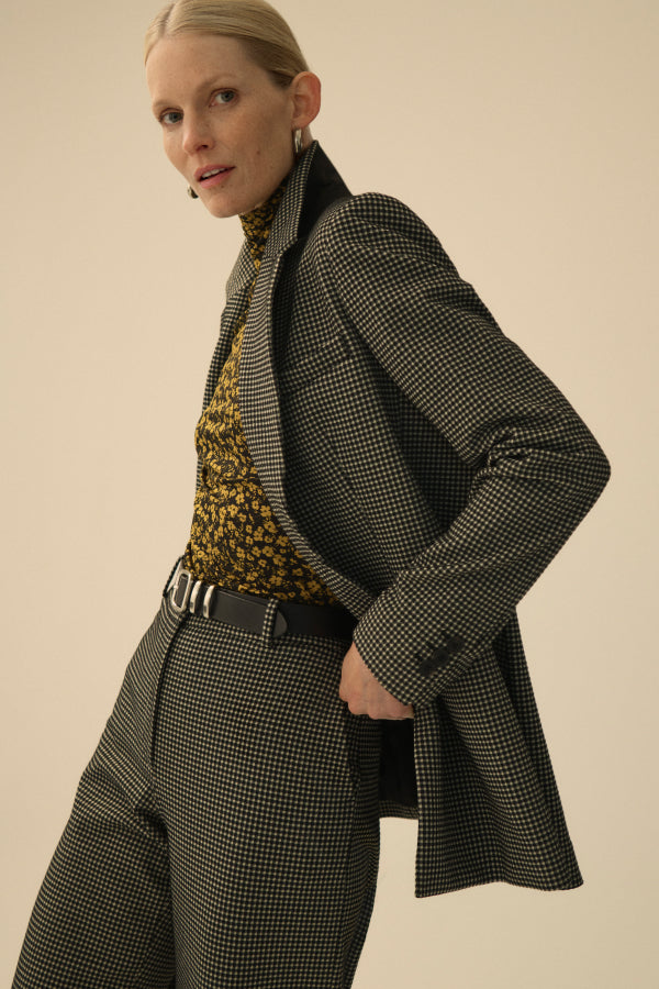 Woman wearing a gray checkered coat and pants with a patterned top against a beige background