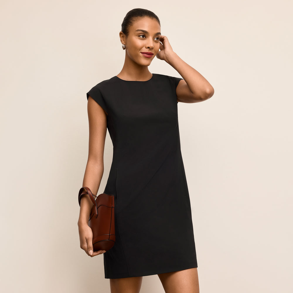 Woman wearing a black dress holding a brown handbag against a beige background