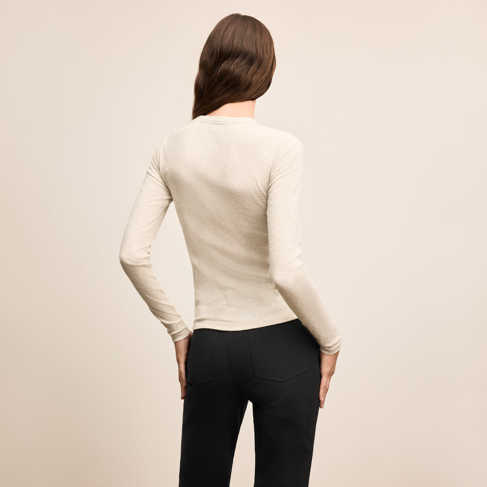 Person wearing a beige long-sleeve top and black pants on a beige background