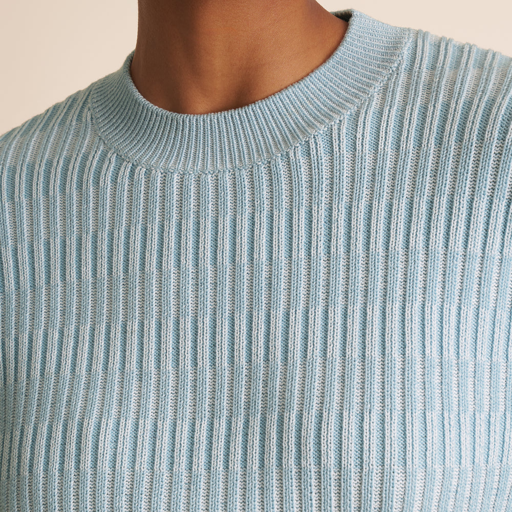Close-up of a person wearing a light blue ribbed sweater against a neutral background
