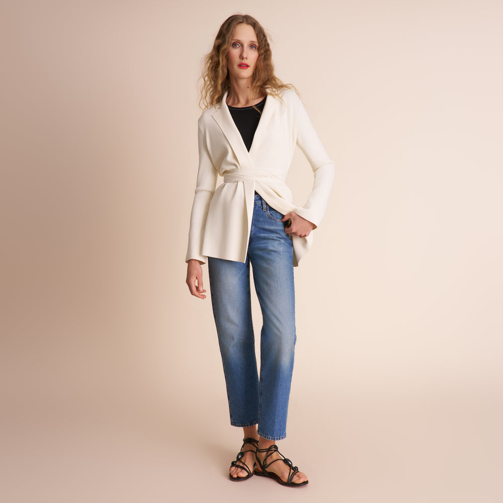 Woman wearing a white blazer and blue jeans on a beige background