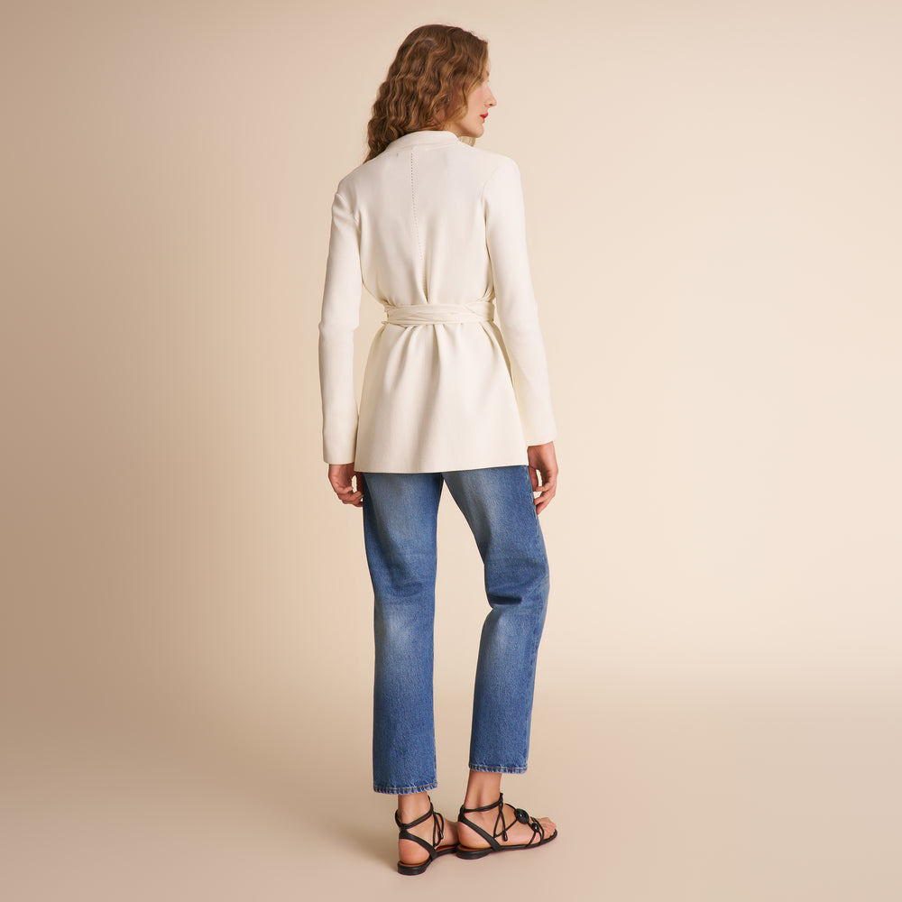 Woman wearing a white coat and blue jeans on a beige background