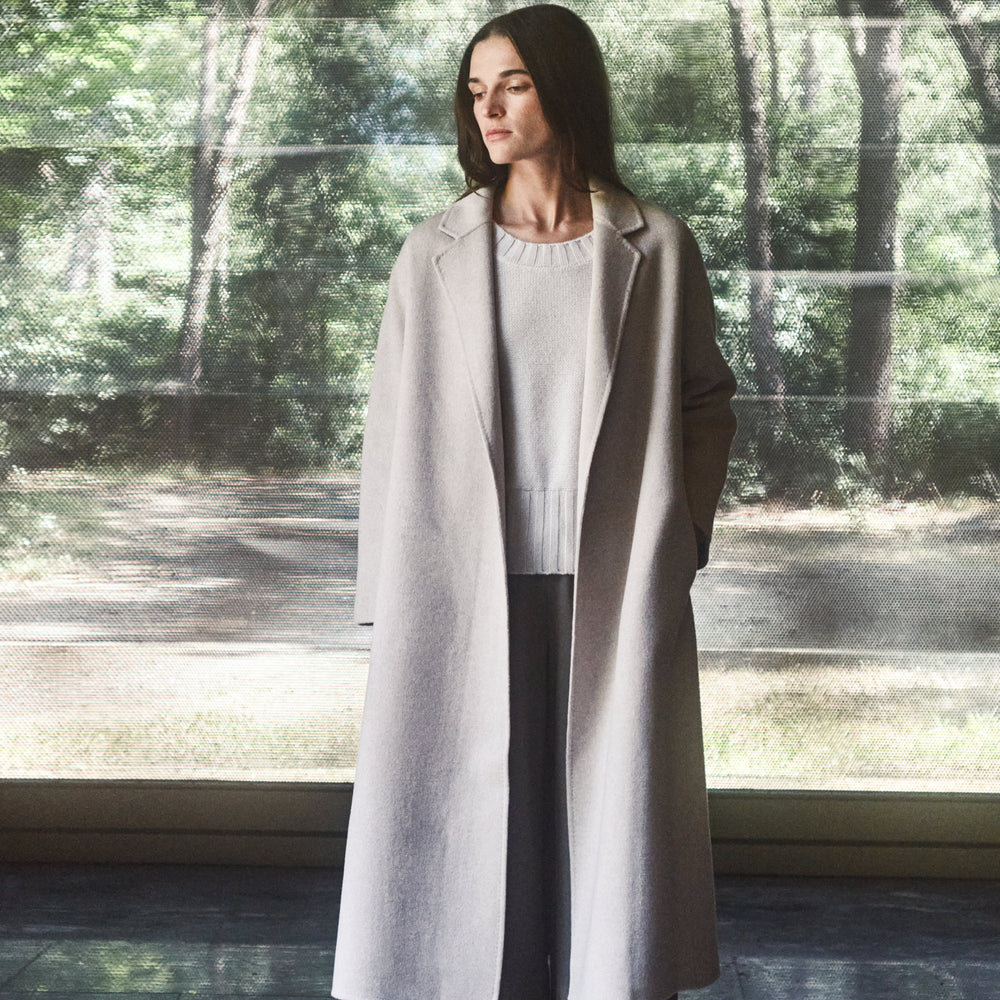 Woman wearing a long coat standing in front of a reflective surface with a forest background
