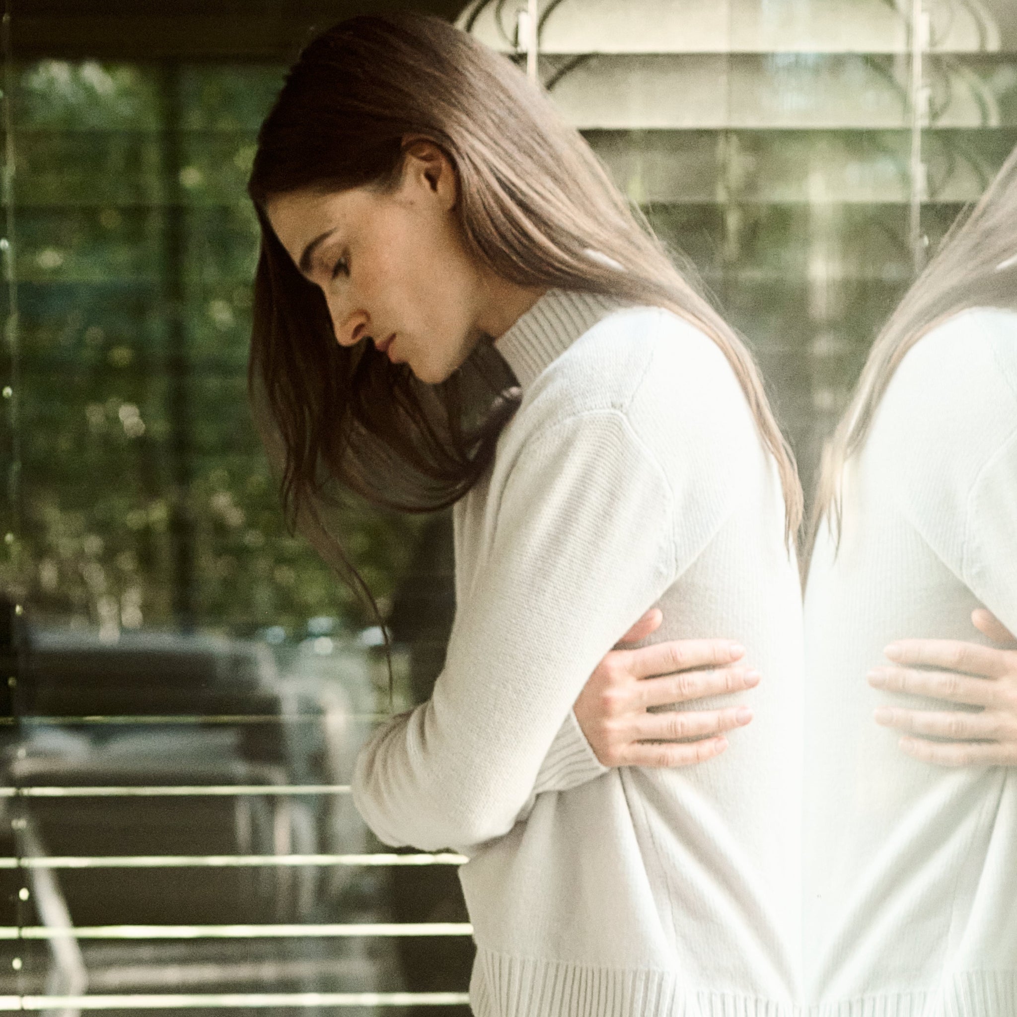 Woman in a white sweater standing in front of a glass door with reflections.