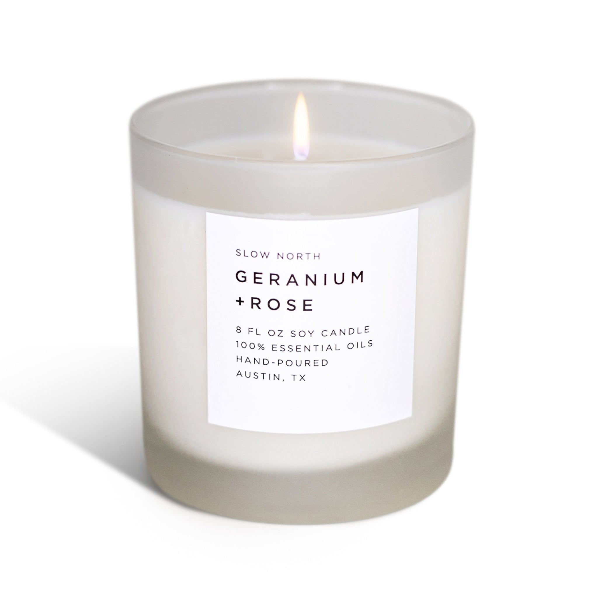 Frosted candle with a label reading 'Slow North Geranium + Rose' on a white background 