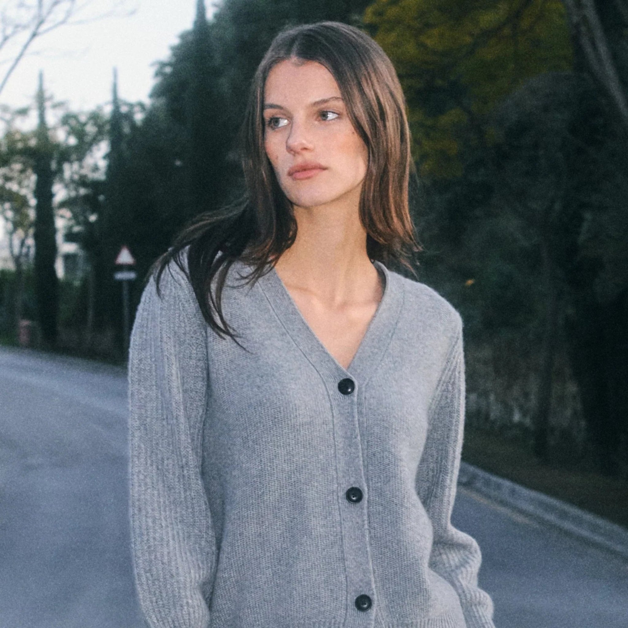 Woman wearing a gray cardigan on a road with trees in the background 
