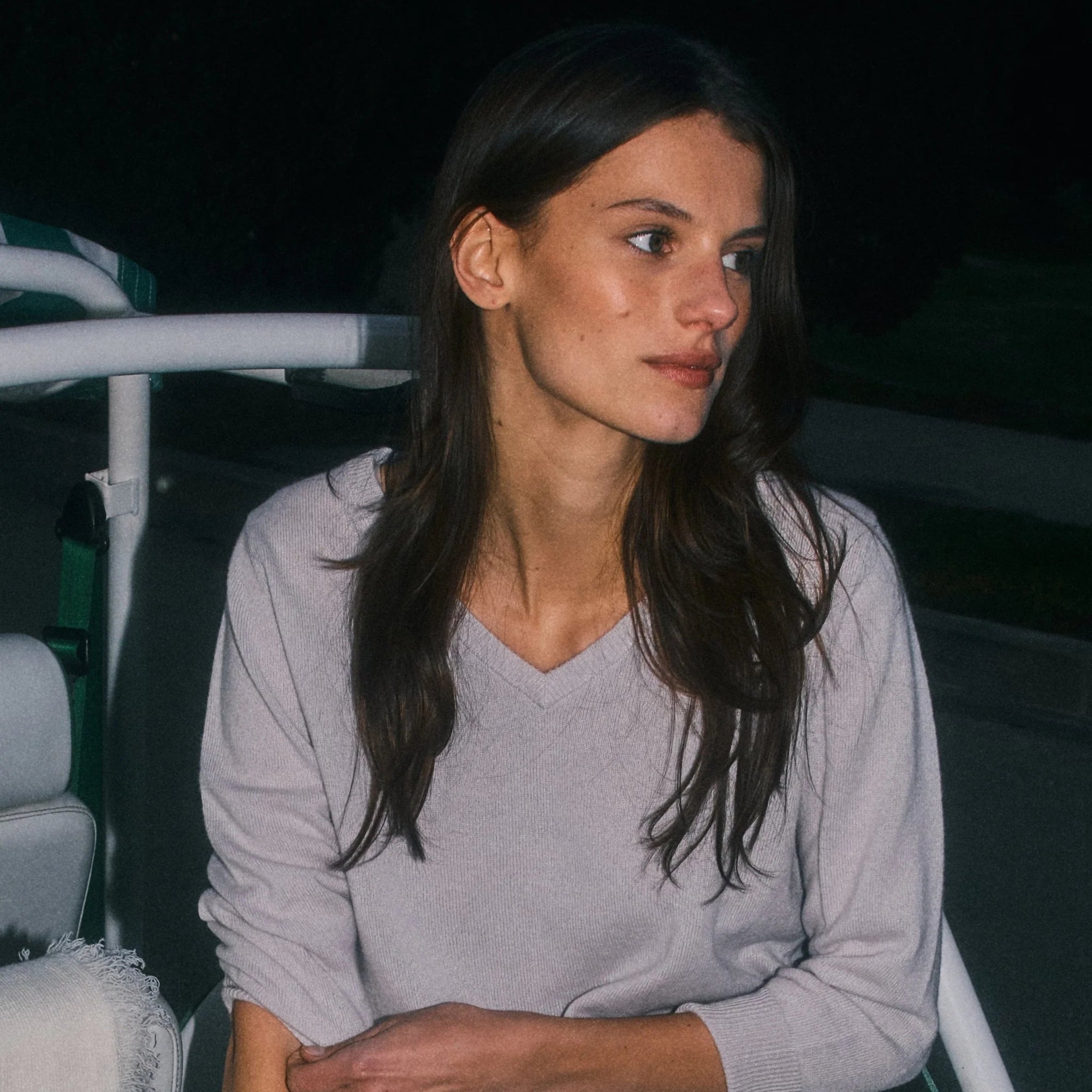 Woman wearing a gray sweater and white pants sitting on a boat at night.
