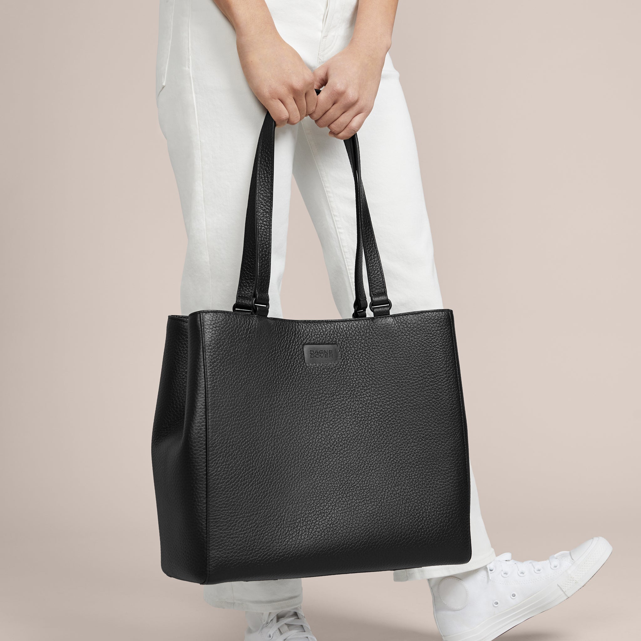 Person holding a black leather tote bag against a neutral background