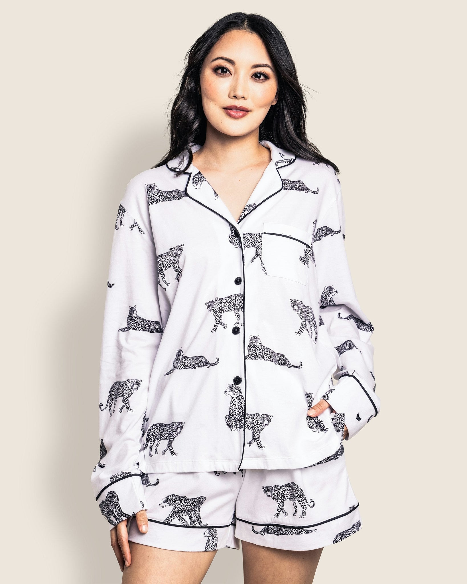 Woman wearing a white pajama set with black animal prints against a beige background 