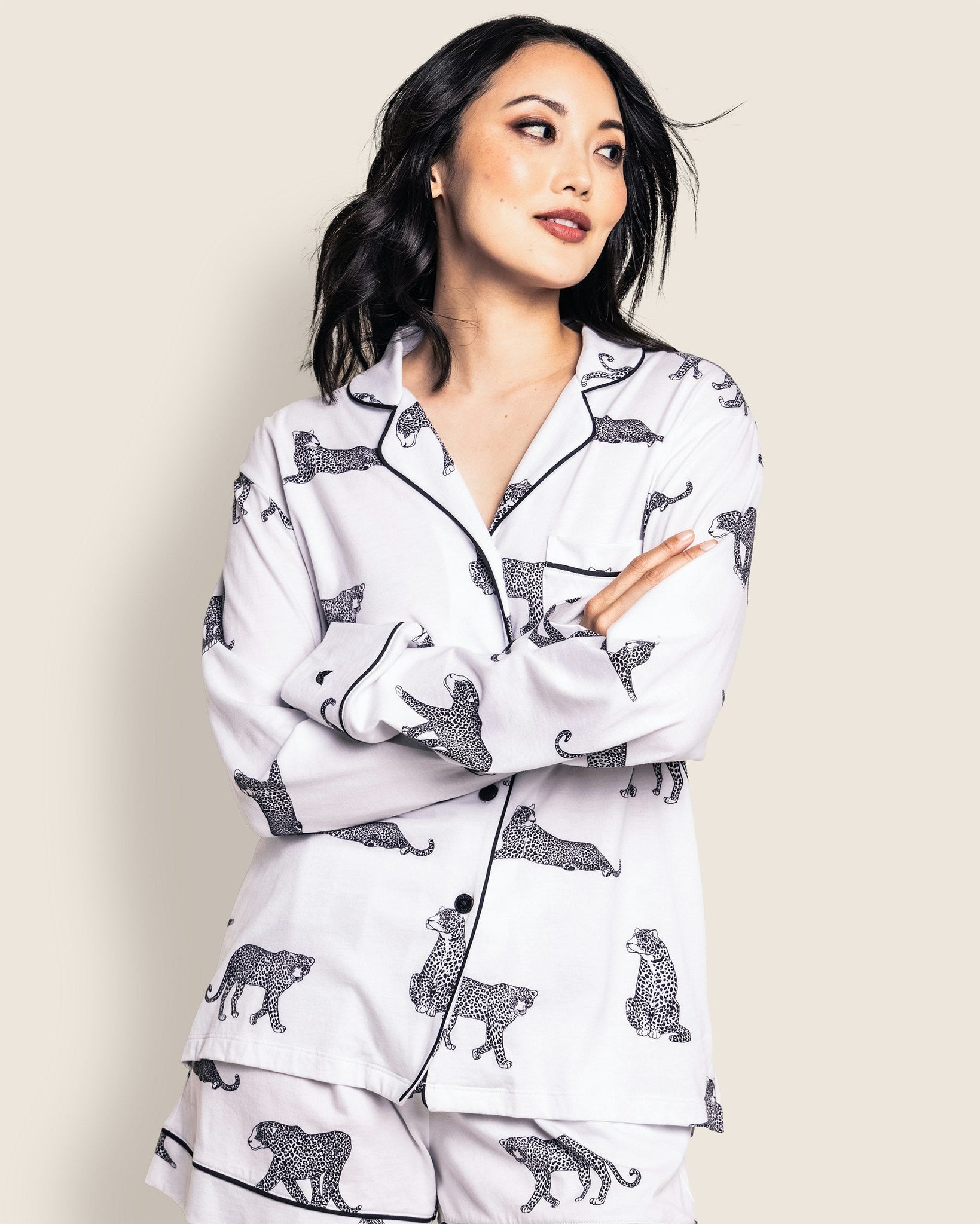 Woman wearing a white pajama set with black animal prints against a beige background