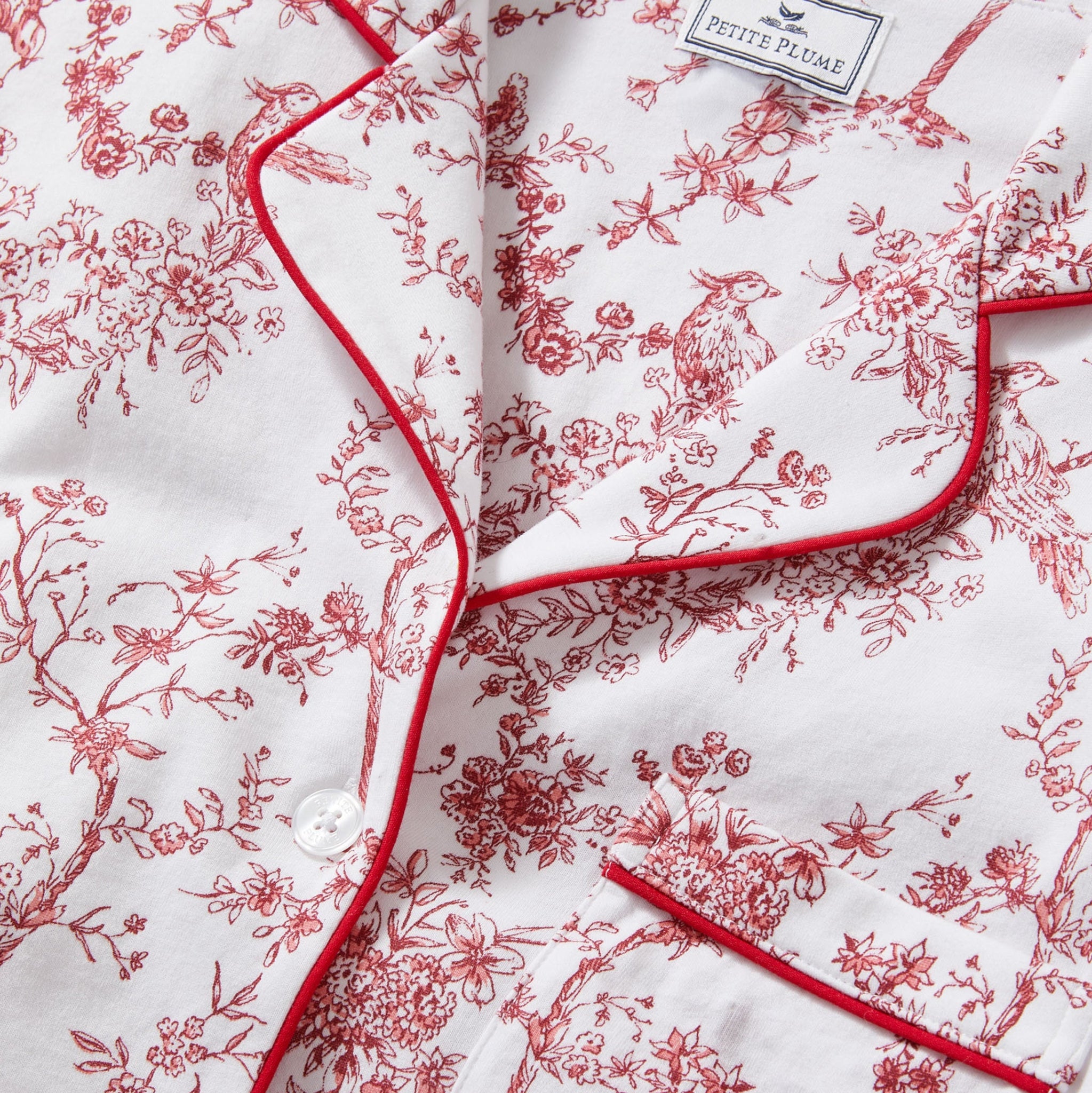 Red floral pattern on white fabric with 'Petite Plume' branding.