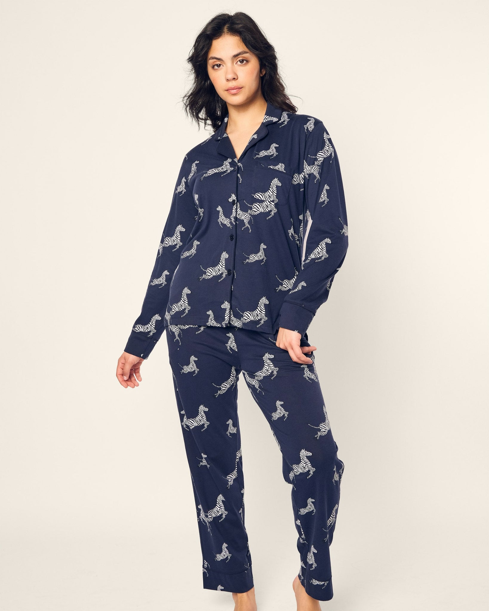 Woman wearing a navy blue pajama set with white animal prints on a plain background