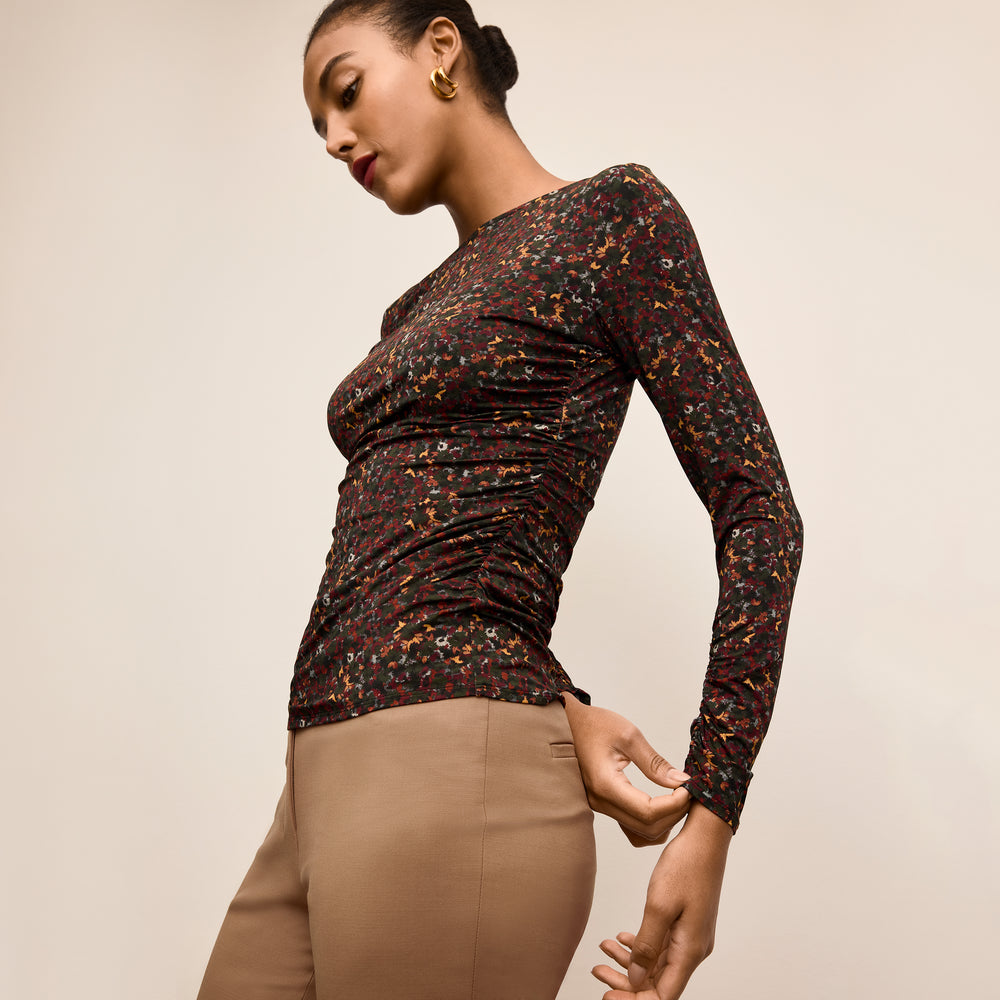 Woman wearing a patterned long-sleeve top and beige pants on a beige background
