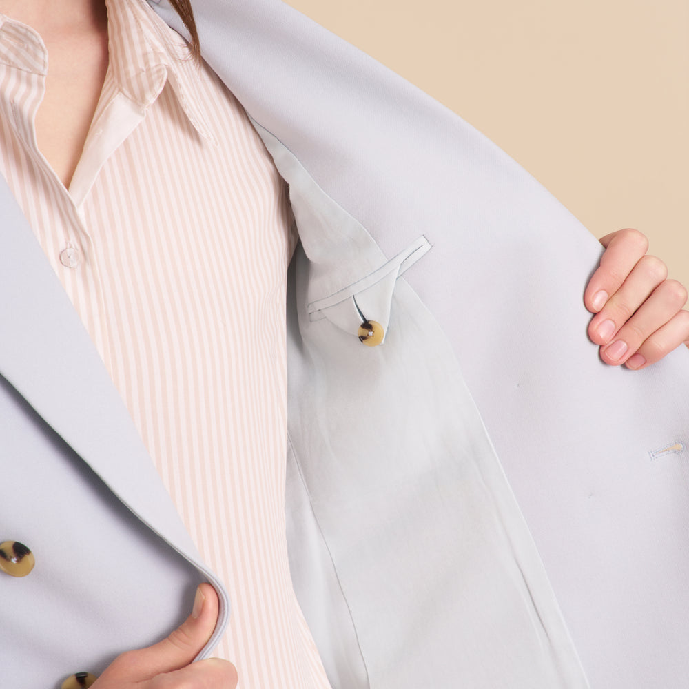 Woman wearing a light blue blazer and matching pants on a beige background