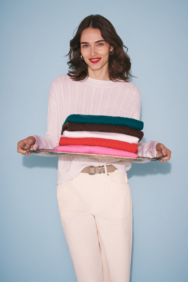 Three cable knit sweaters in pink, burgundy, and red on top of each other in the grass.
