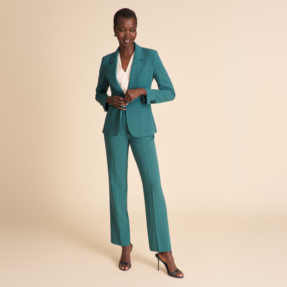 Woman wearing a white top and teal pants on a beige background