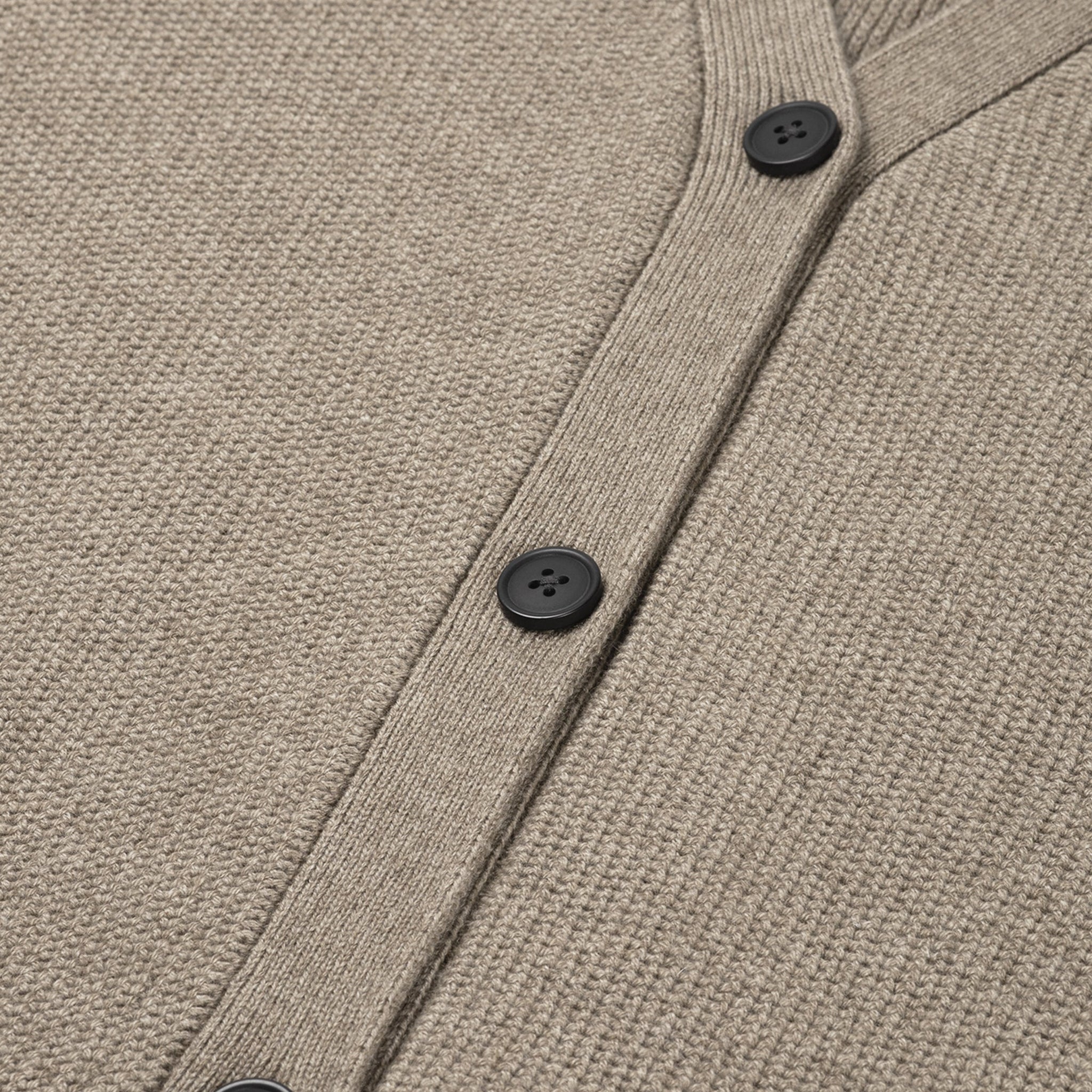 Close-up of a beige cardigan with black buttons on a matching fabric background