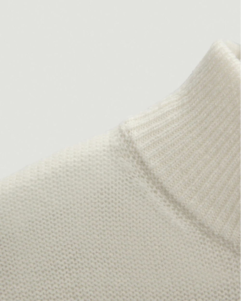 Close-up of a textured beige sweater on a light gray background.