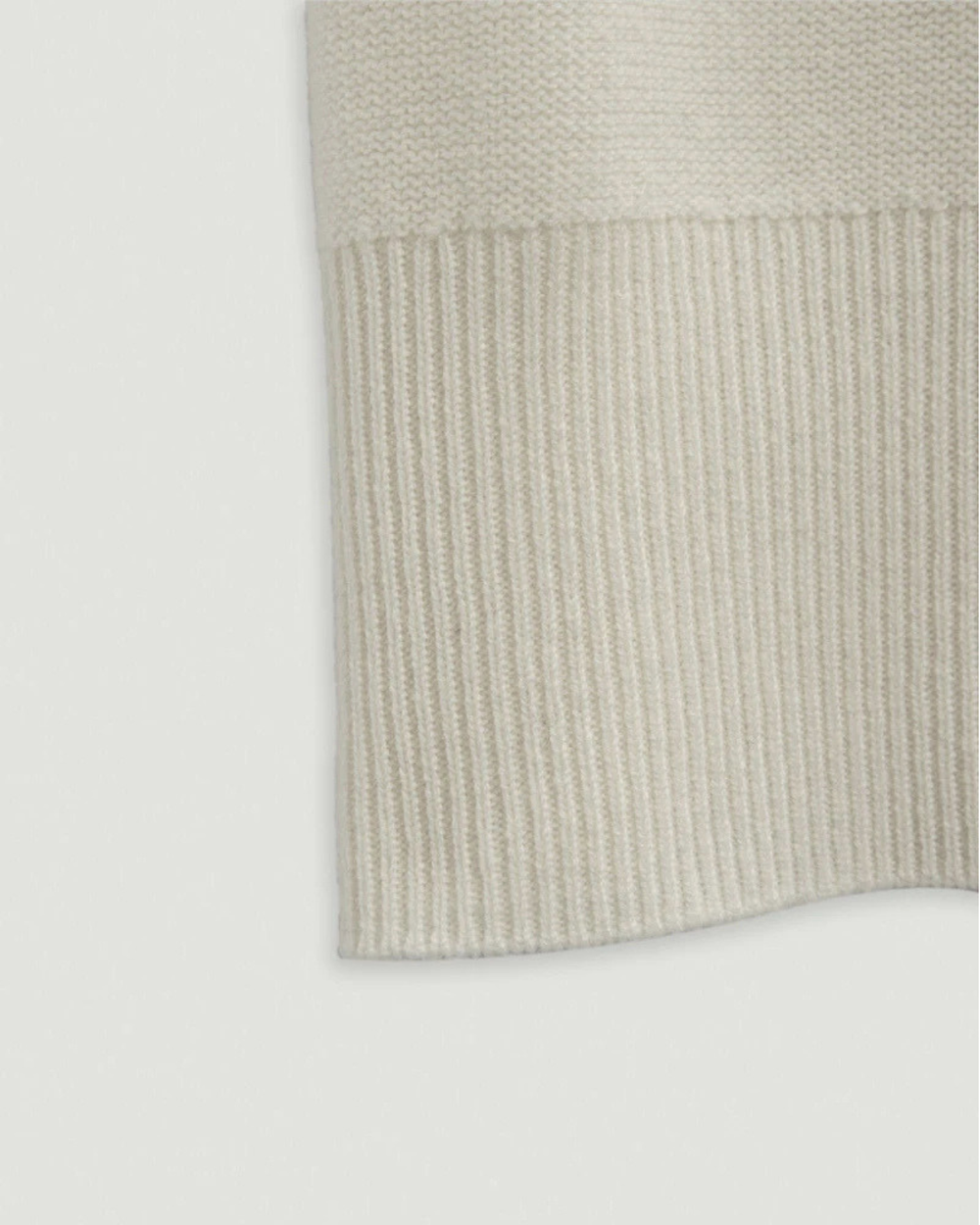 Close-up of a beige knitted sweater on a light gray background.