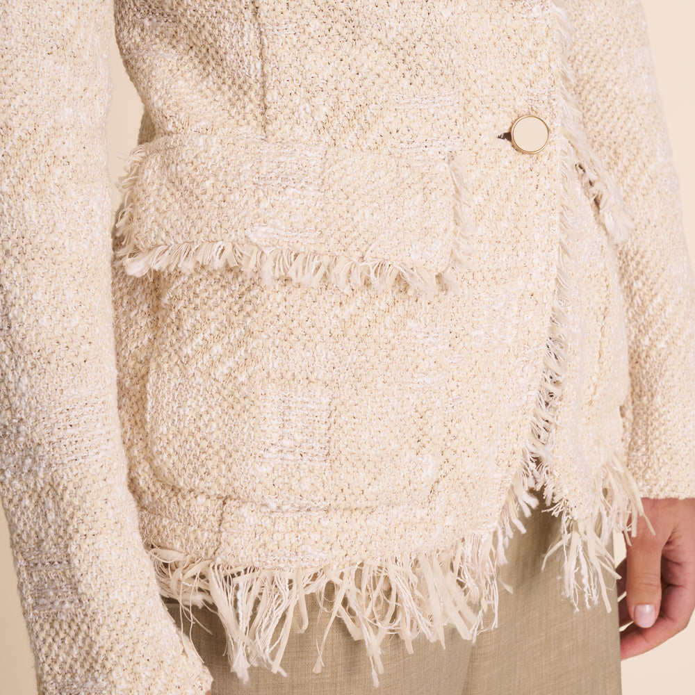 Close-up of a textured beige sweater with fringes and a button.
