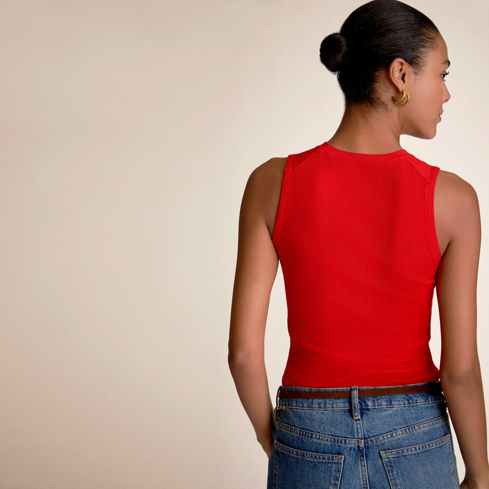Woman wearing a red sleeveless top and blue jeans on a beige background