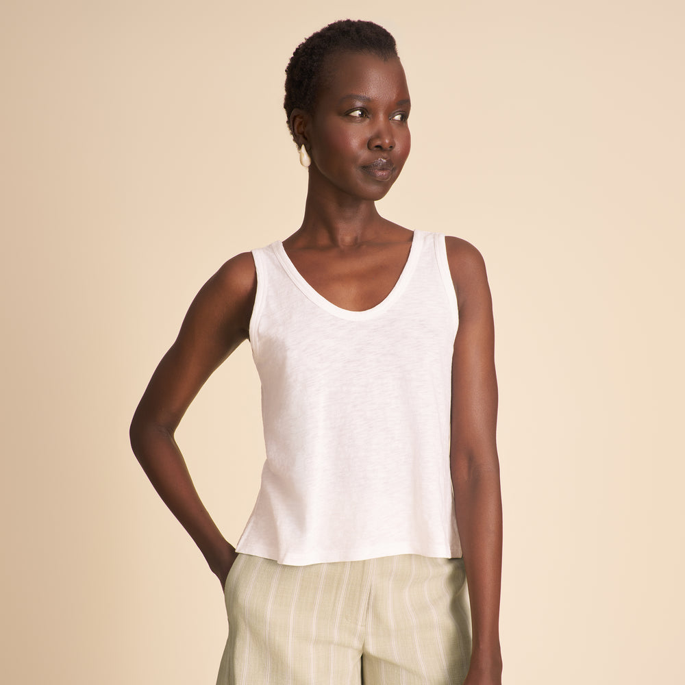 Woman wearing a white tank top with striped beige and mauve shorts on a beige background