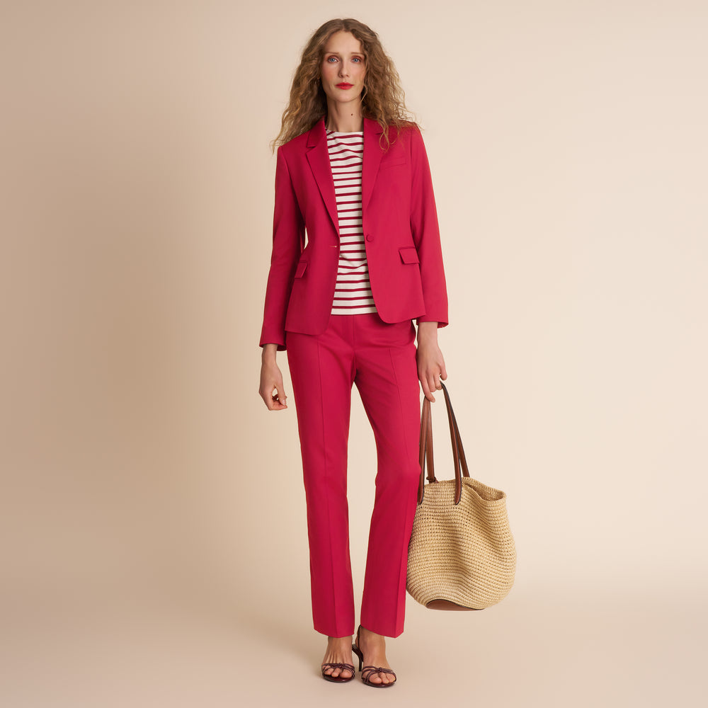 Woman wearing a red suit holding a beige handbag against a beige background
