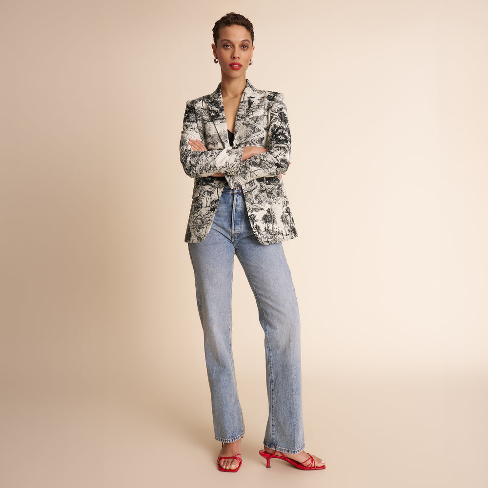 Woman wearing a patterned blazer and jeans on a beige background