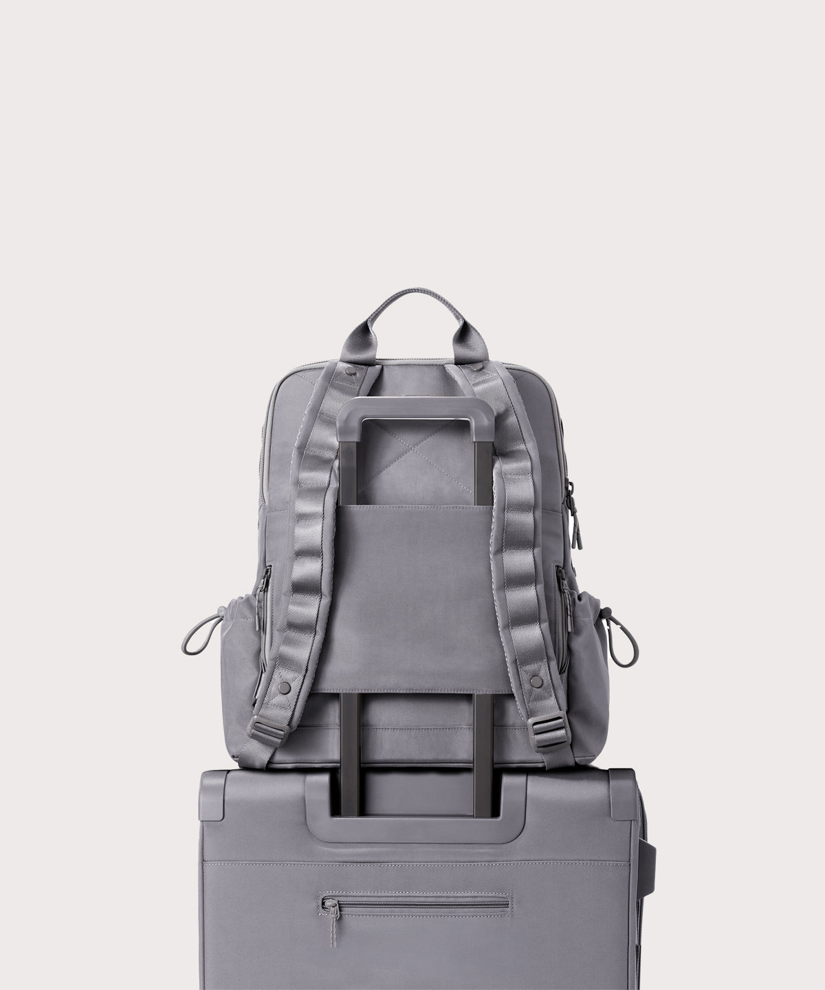 Gray backpack on top of a gray suitcase against a white background