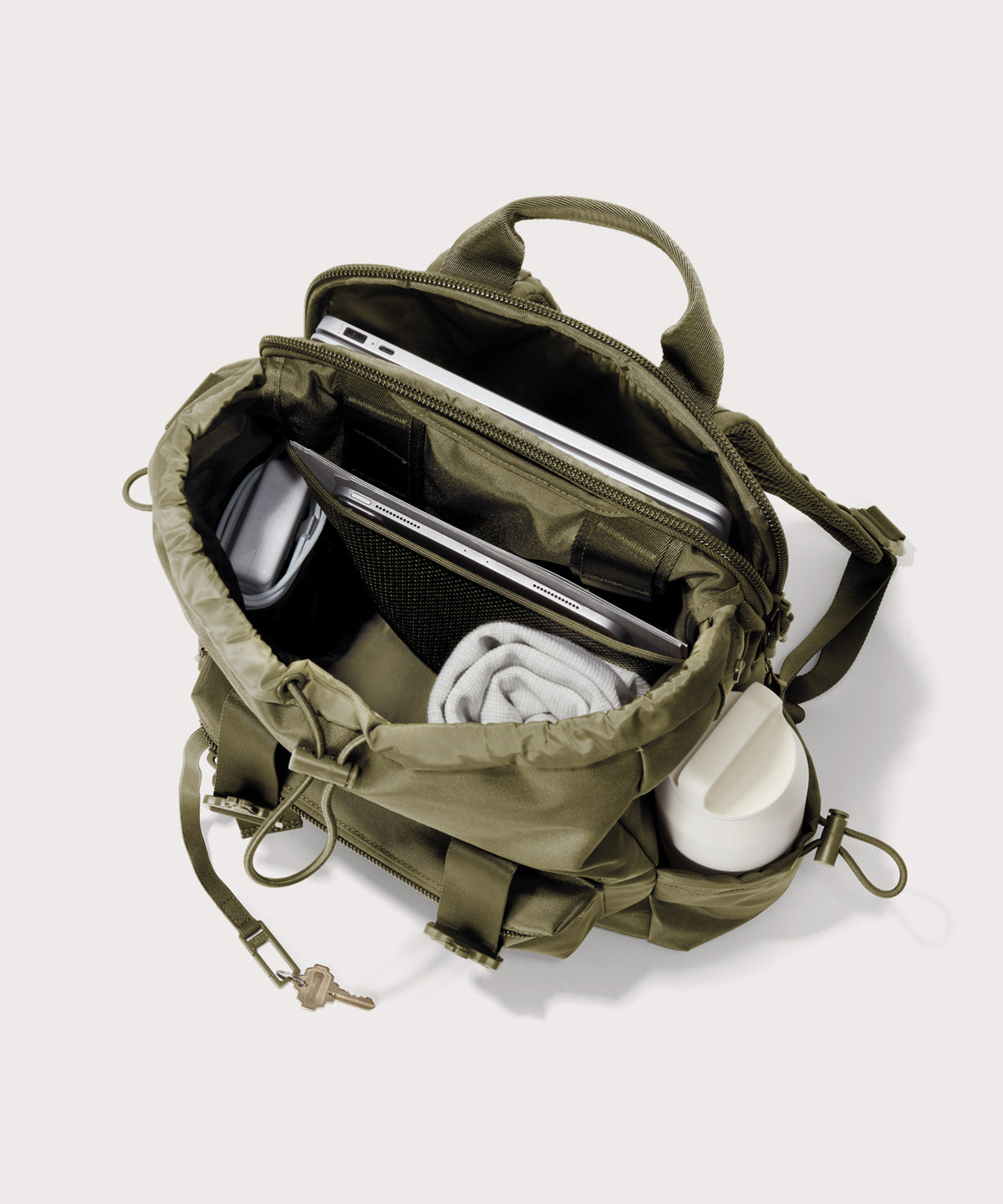 Green backpack with compartments containing electronic devices and personal items on a white background 