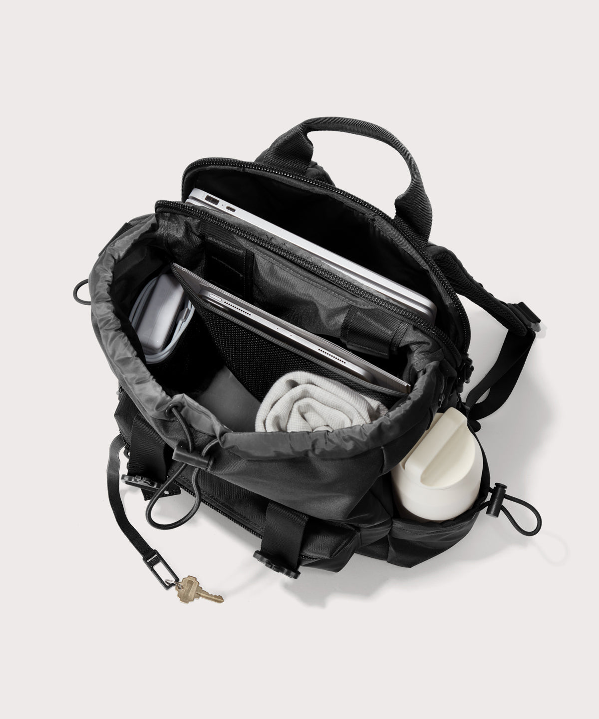 Black backpack with compartments containing a phone, wallet, and other items on a light gray background